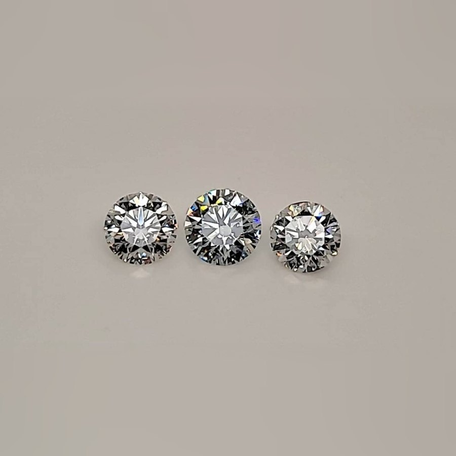 Three round brilliant diamonds, loose, on a grey background