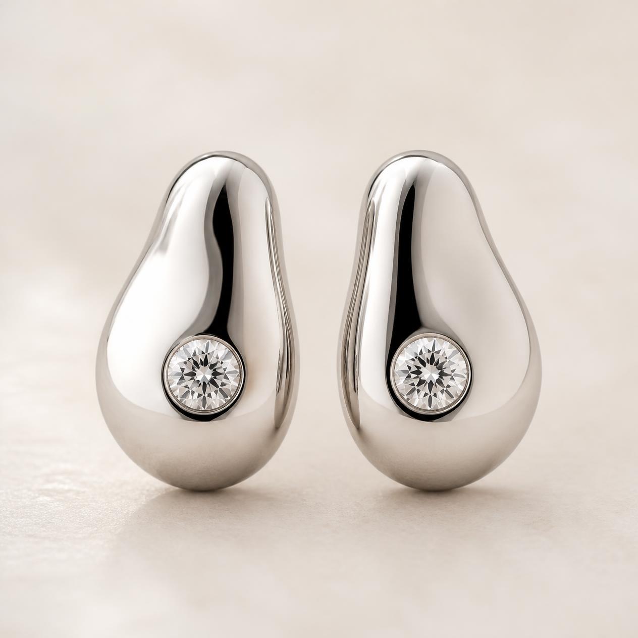 Sculptural polished platinum pebble earrings each set with a round diamond
